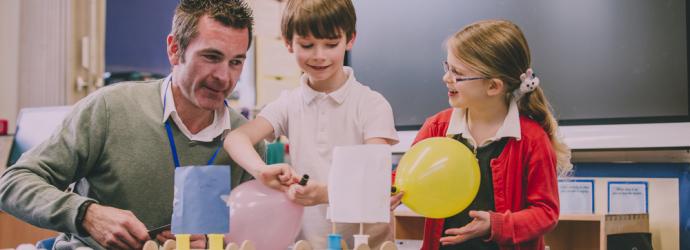 Male teacher supporting two primary school children in a lesson