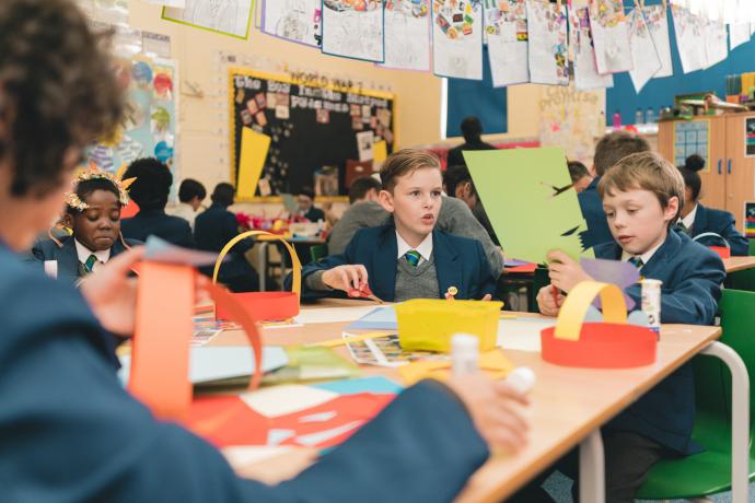 Image shows children of primary school age cutting up coloured card to make head dresses